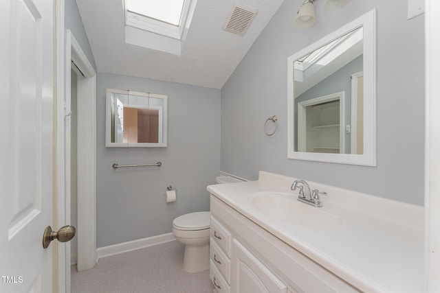 bathroom featuring vaulted ceiling with skylight, vanity, toilet, and a textured ceiling