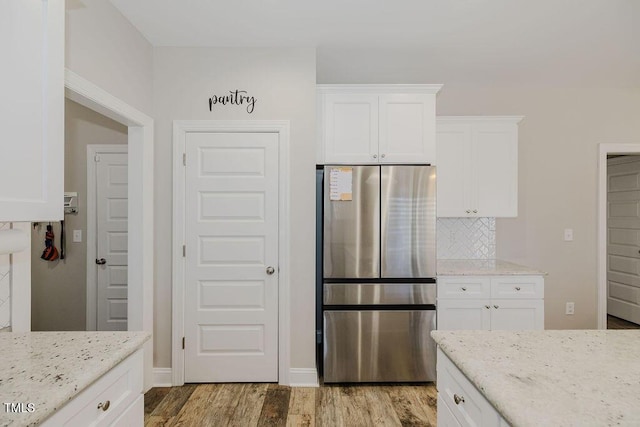 kitchen with stainless steel fridge, light hardwood / wood-style flooring, white cabinetry, light stone counters, and decorative backsplash