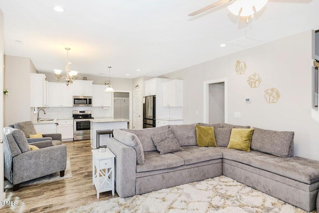 living room featuring sink, ceiling fan with notable chandelier, and light hardwood / wood-style flooring