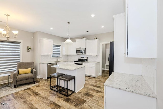 kitchen with sink, appliances with stainless steel finishes, hanging light fixtures, a center island, and white cabinets