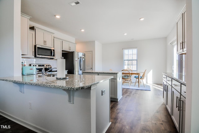 kitchen featuring light stone counters, appliances with stainless steel finishes, a kitchen breakfast bar, and tasteful backsplash