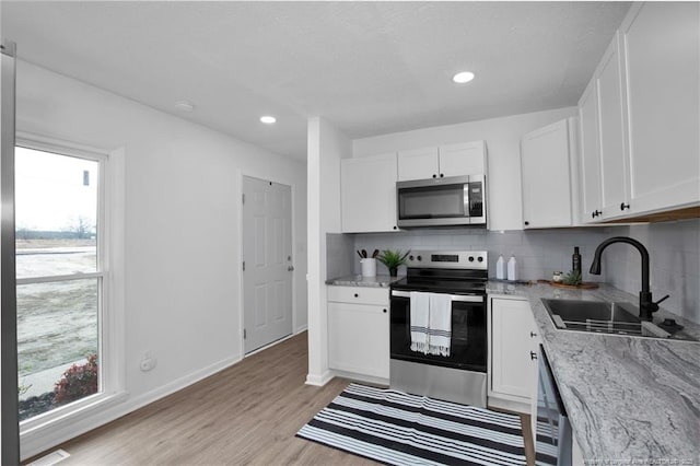 kitchen with sink, light wood-type flooring, appliances with stainless steel finishes, light stone counters, and white cabinetry