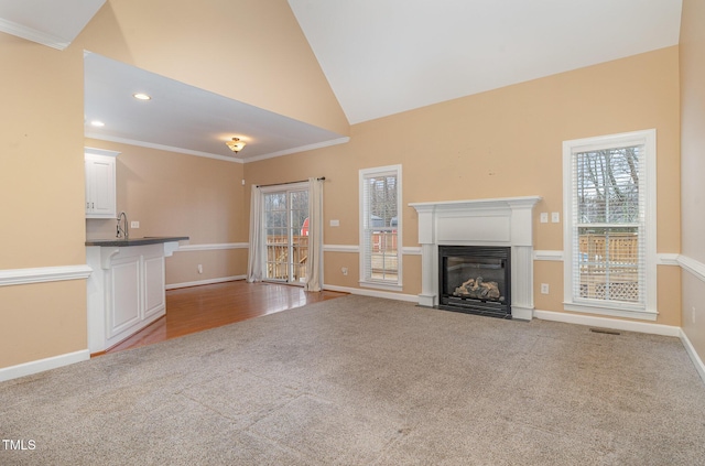 unfurnished living room featuring sink, high vaulted ceiling, crown molding, and light colored carpet