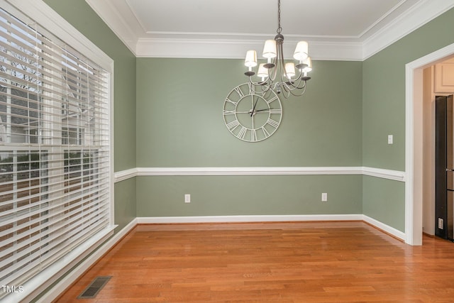 unfurnished dining area featuring wood-type flooring, crown molding, and a chandelier