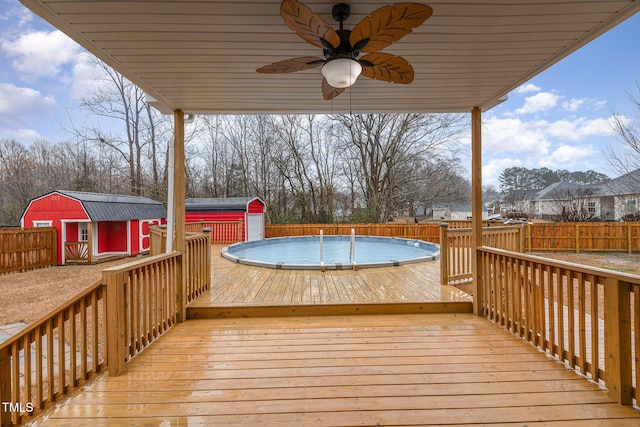 deck featuring ceiling fan, a fenced in pool, and a shed