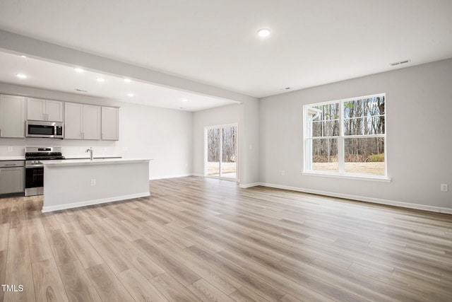 kitchen with sink, a center island with sink, stainless steel appliances, and light wood-type flooring