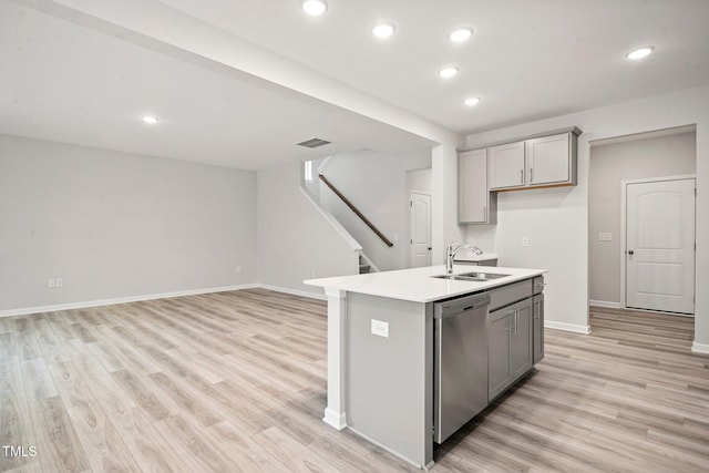 kitchen with gray cabinetry, dishwasher, sink, a center island with sink, and light wood-type flooring