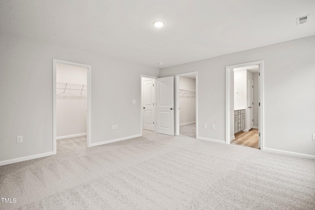 unfurnished bedroom featuring connected bathroom, a spacious closet, a closet, and light colored carpet