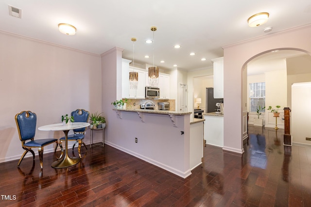 kitchen featuring white cabinetry, stainless steel appliances, kitchen peninsula, decorative light fixtures, and a kitchen bar