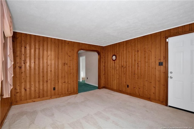 carpeted empty room featuring a textured ceiling, crown molding, and wooden walls