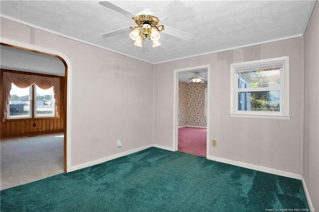 empty room featuring ceiling fan, a healthy amount of sunlight, carpet floors, and crown molding