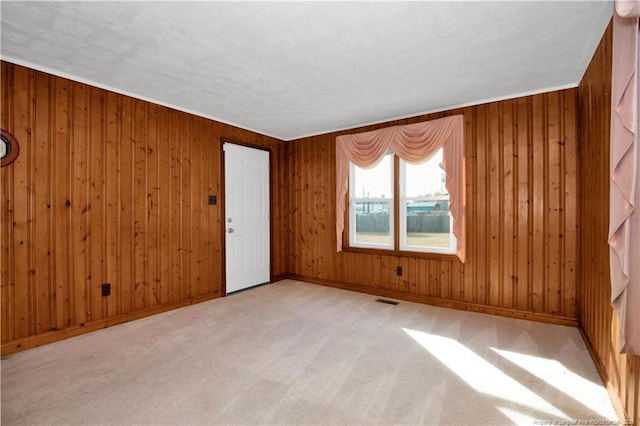 unfurnished room featuring a textured ceiling, light colored carpet, and wood walls