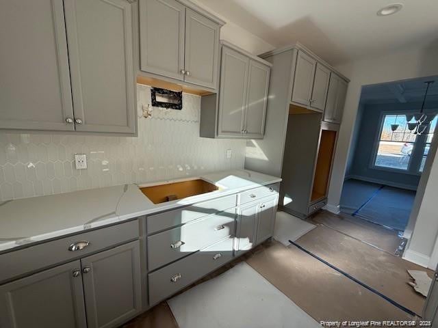 kitchen with a sink, gray cabinets, backsplash, and light countertops