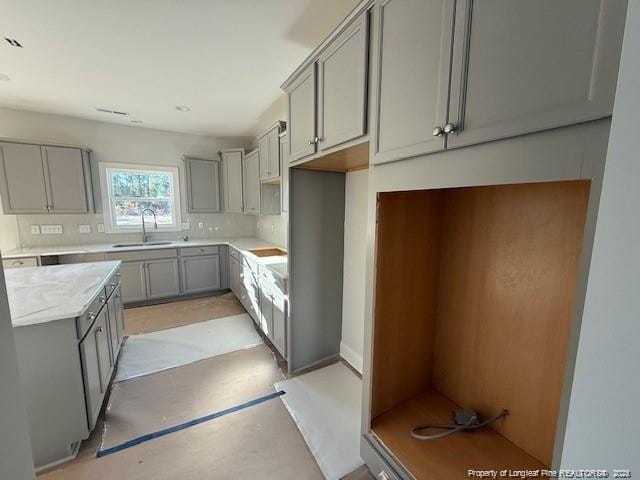 kitchen featuring concrete flooring, gray cabinetry, a sink, light countertops, and decorative backsplash