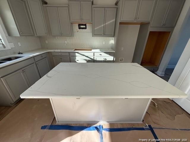 kitchen featuring light stone countertops, gray cabinetry, a sink, a kitchen island, and decorative backsplash