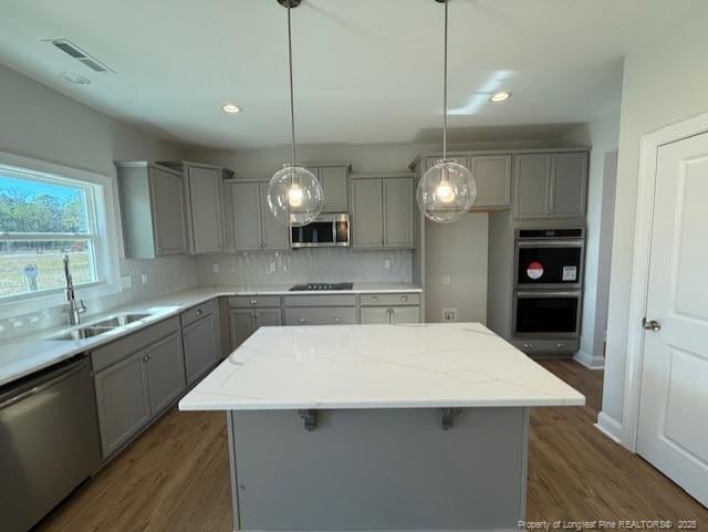 kitchen featuring dark wood finished floors, decorative backsplash, gray cabinetry, appliances with stainless steel finishes, and a sink