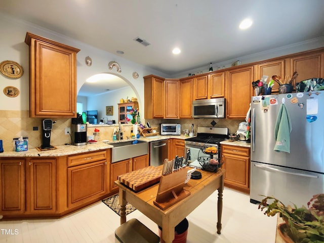 kitchen with sink, decorative backsplash, ornamental molding, light stone counters, and stainless steel appliances