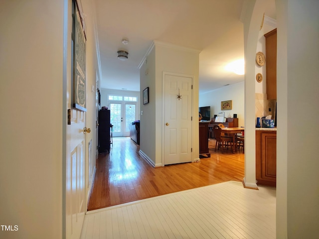 corridor with crown molding, french doors, and light wood-type flooring