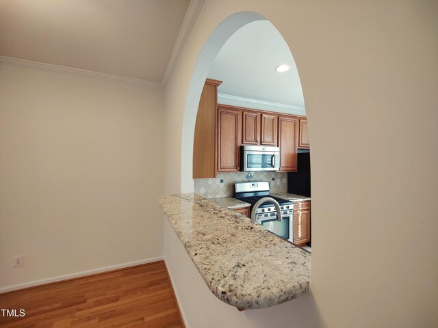 kitchen with a peninsula, baseboards, appliances with stainless steel finishes, backsplash, and crown molding