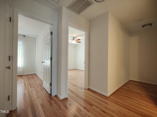 hall with light wood-style flooring, visible vents, and baseboards