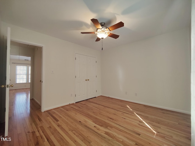 unfurnished bedroom with a closet, attic access, ceiling fan, light wood-type flooring, and baseboards