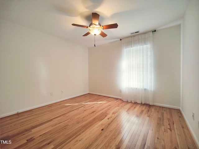 spare room with light wood-type flooring, ceiling fan, visible vents, and baseboards