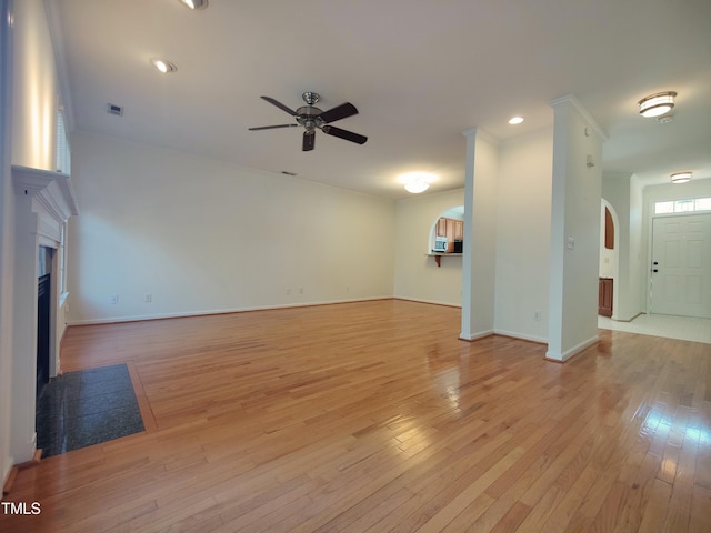 unfurnished living room with arched walkways, ceiling fan, a fireplace with flush hearth, visible vents, and light wood finished floors