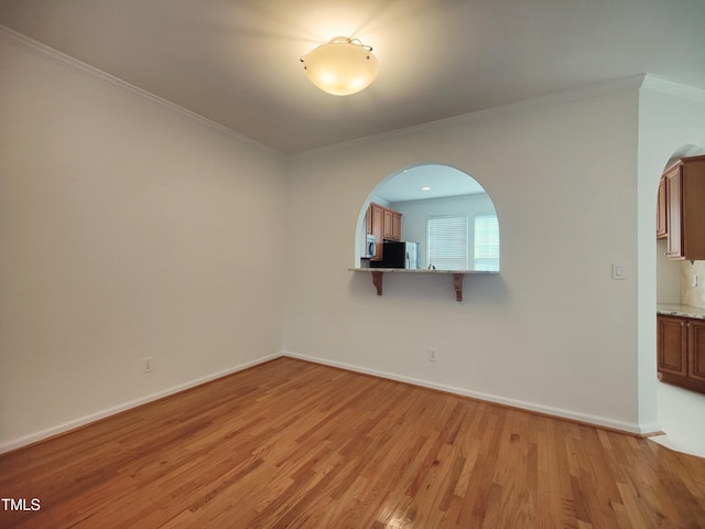 spare room featuring light wood-type flooring, baseboards, arched walkways, and crown molding