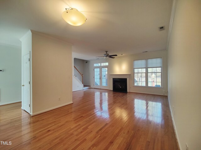 unfurnished living room featuring a fireplace, light wood finished floors, visible vents, stairway, and ornamental molding