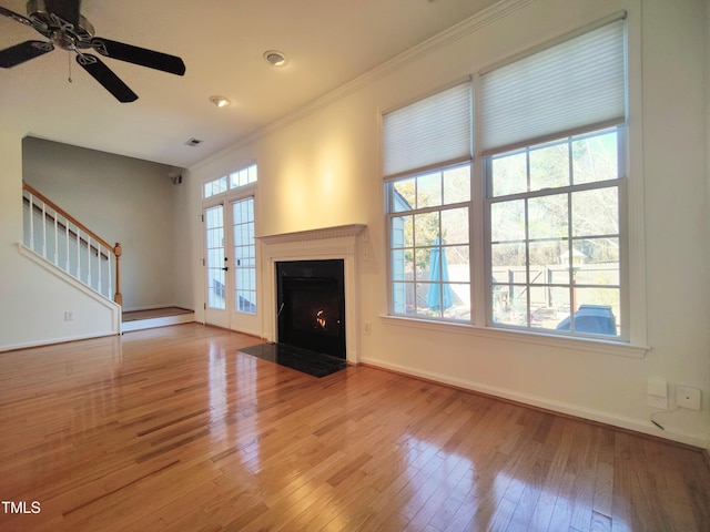 unfurnished living room with light wood-style floors, a fireplace with flush hearth, stairs, and ornamental molding