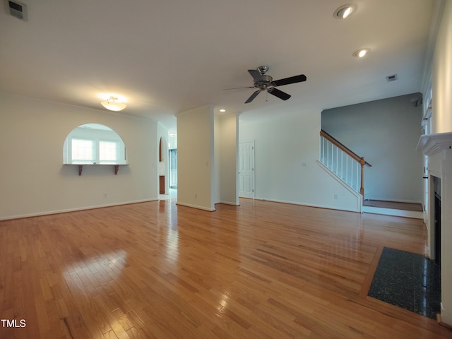 unfurnished living room featuring a fireplace with flush hearth, visible vents, a ceiling fan, stairway, and light wood finished floors