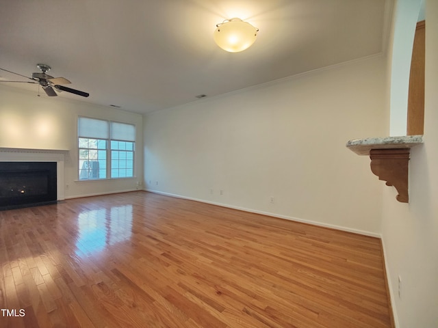 unfurnished living room with ceiling fan, a fireplace with flush hearth, baseboards, ornamental molding, and light wood-type flooring