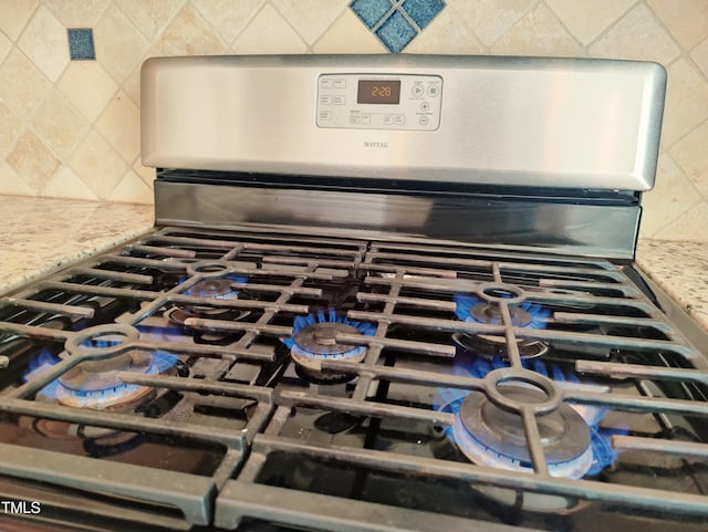 details with stainless steel gas stove, decorative backsplash, and light stone countertops