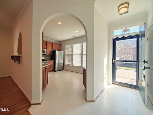 foyer entrance featuring arched walkways, light wood-style floors, visible vents, and crown molding