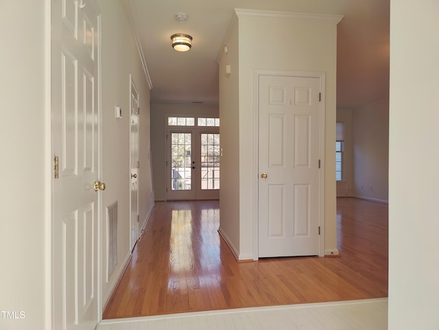 corridor with light wood-style floors, visible vents, crown molding, and french doors