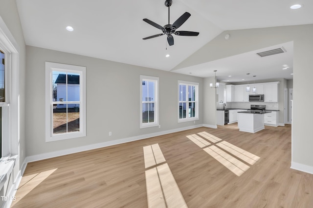 unfurnished living room with ceiling fan with notable chandelier, vaulted ceiling, and light hardwood / wood-style flooring