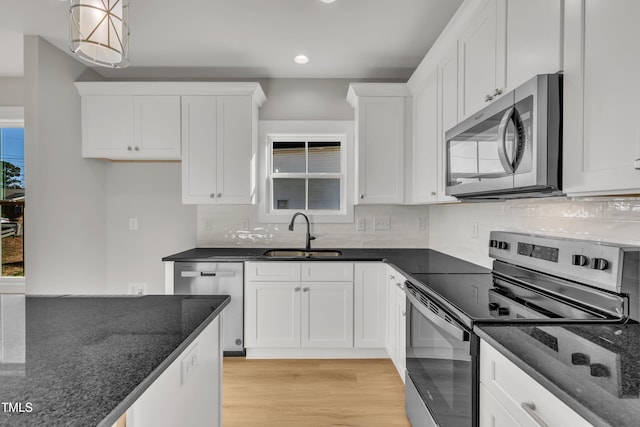 kitchen with white cabinets, appliances with stainless steel finishes, decorative light fixtures, and dark stone counters