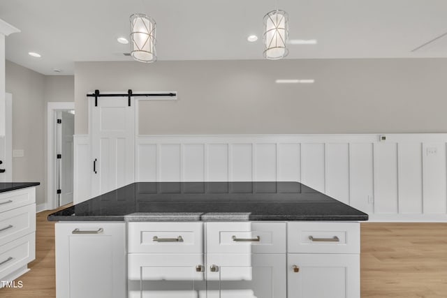 kitchen with a barn door, decorative light fixtures, white cabinetry, and light hardwood / wood-style flooring