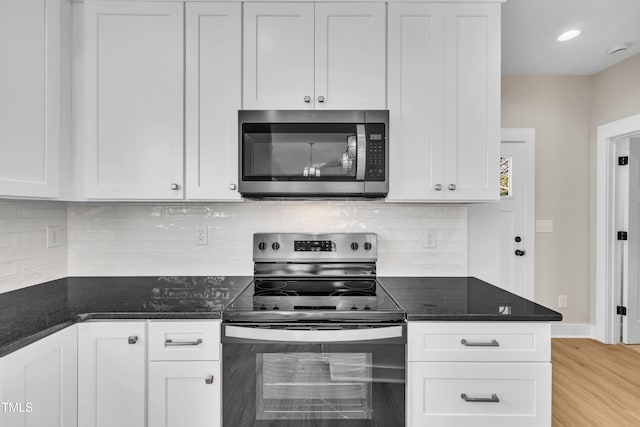 kitchen featuring dark stone countertops, white cabinetry, light hardwood / wood-style floors, and appliances with stainless steel finishes