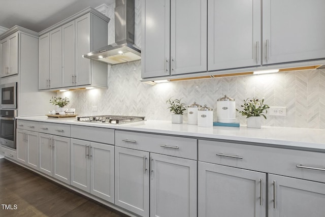 kitchen with stainless steel appliances, gray cabinets, wall chimney range hood, and backsplash