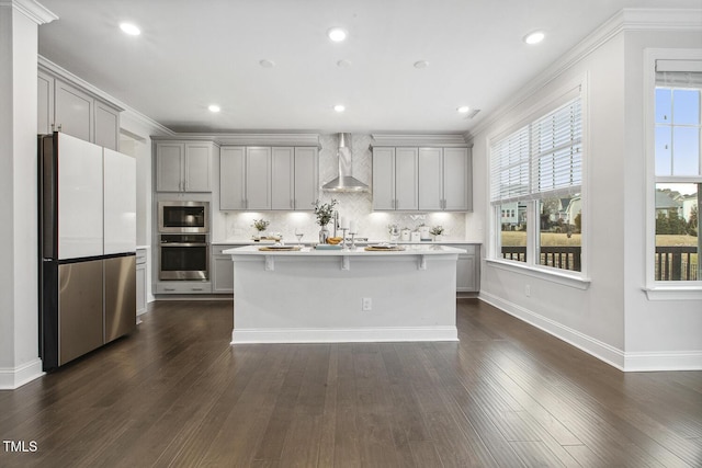 kitchen featuring gray cabinetry, an island with sink, wall chimney exhaust hood, and appliances with stainless steel finishes