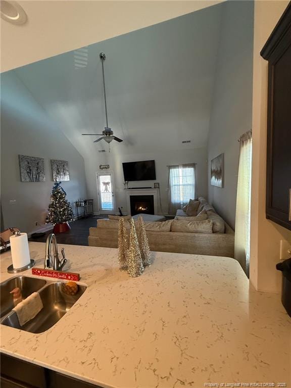 living area with a warm lit fireplace, ceiling fan, and high vaulted ceiling