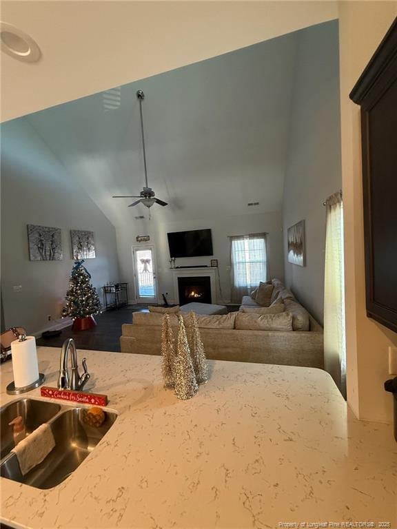 living area with a lit fireplace, high vaulted ceiling, and a ceiling fan