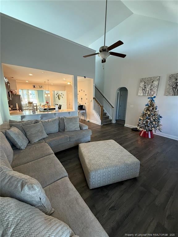 living room with arched walkways, high vaulted ceiling, dark wood-type flooring, baseboards, and stairs