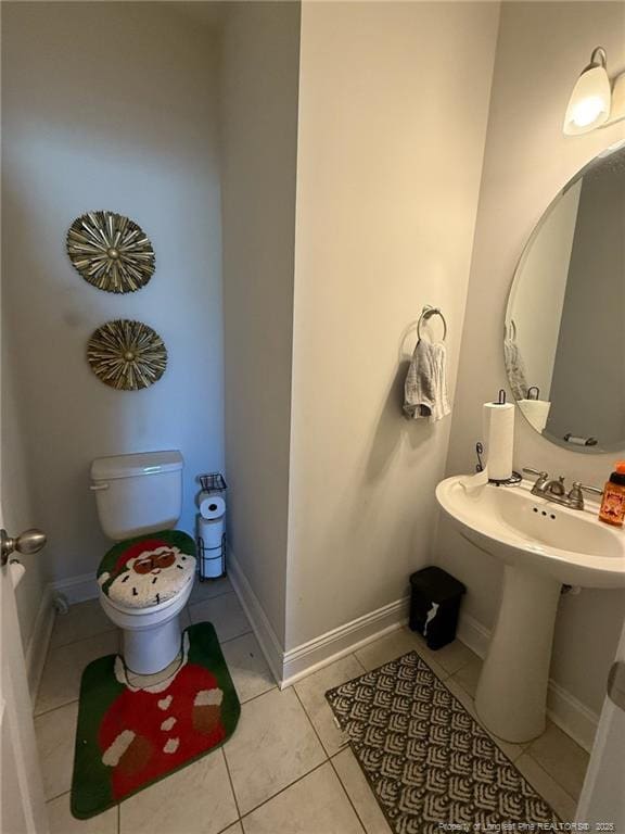 half bath with toilet, baseboards, and tile patterned floors