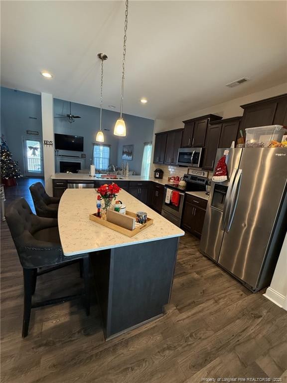 kitchen featuring dark wood-style flooring, a fireplace, stainless steel appliances, visible vents, and hanging light fixtures