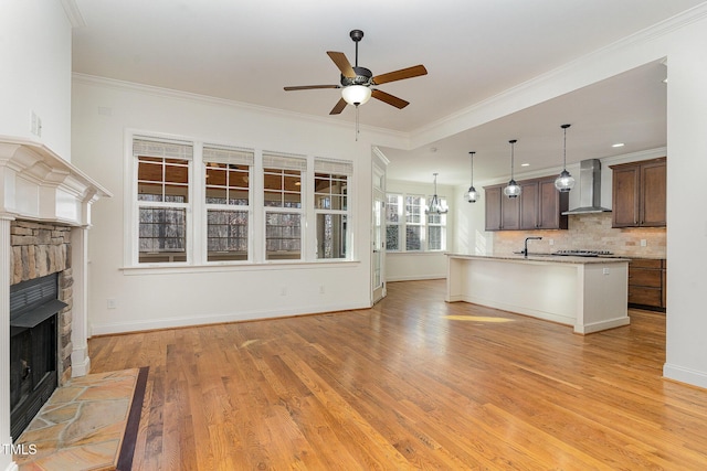 unfurnished living room with ornamental molding, a stone fireplace, ceiling fan with notable chandelier, and light hardwood / wood-style floors