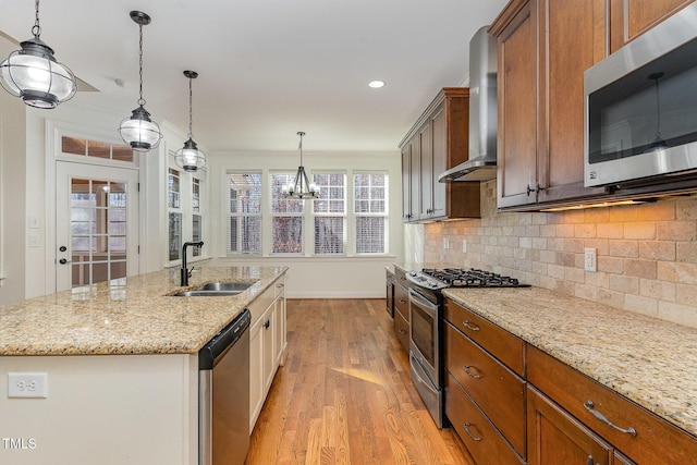 kitchen with sink, appliances with stainless steel finishes, hanging light fixtures, a center island with sink, and wall chimney exhaust hood