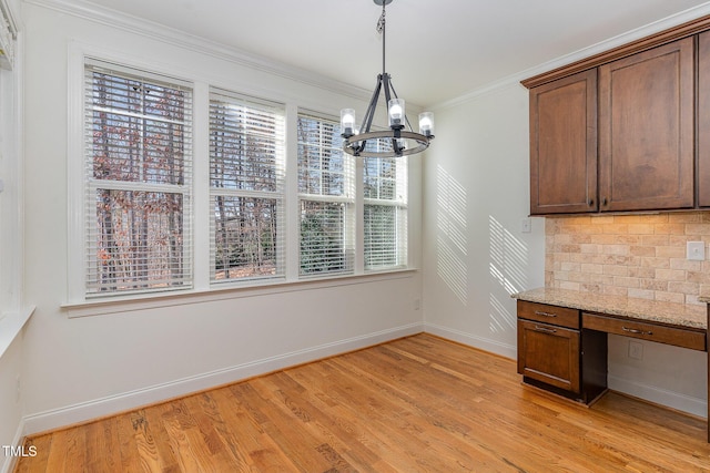 unfurnished dining area featuring ornamental molding, built in desk, an inviting chandelier, and light hardwood / wood-style flooring