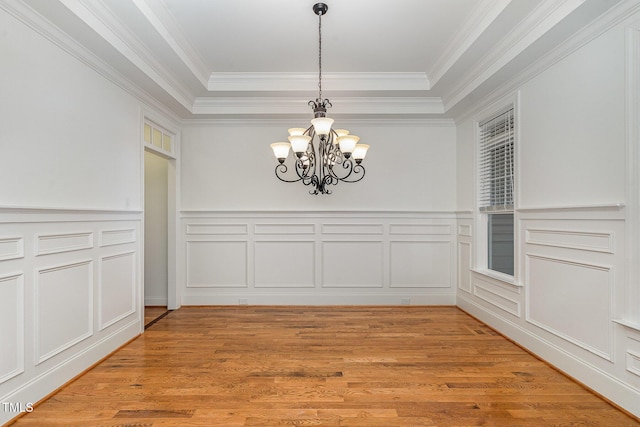 unfurnished dining area with crown molding, a raised ceiling, hardwood / wood-style floors, and a notable chandelier